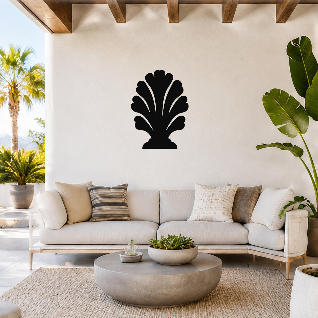 Black metal wall art in a coral or shell silhouette design, mounted on a white wall above a light-colored sofa in a bright, coastal-style living room.