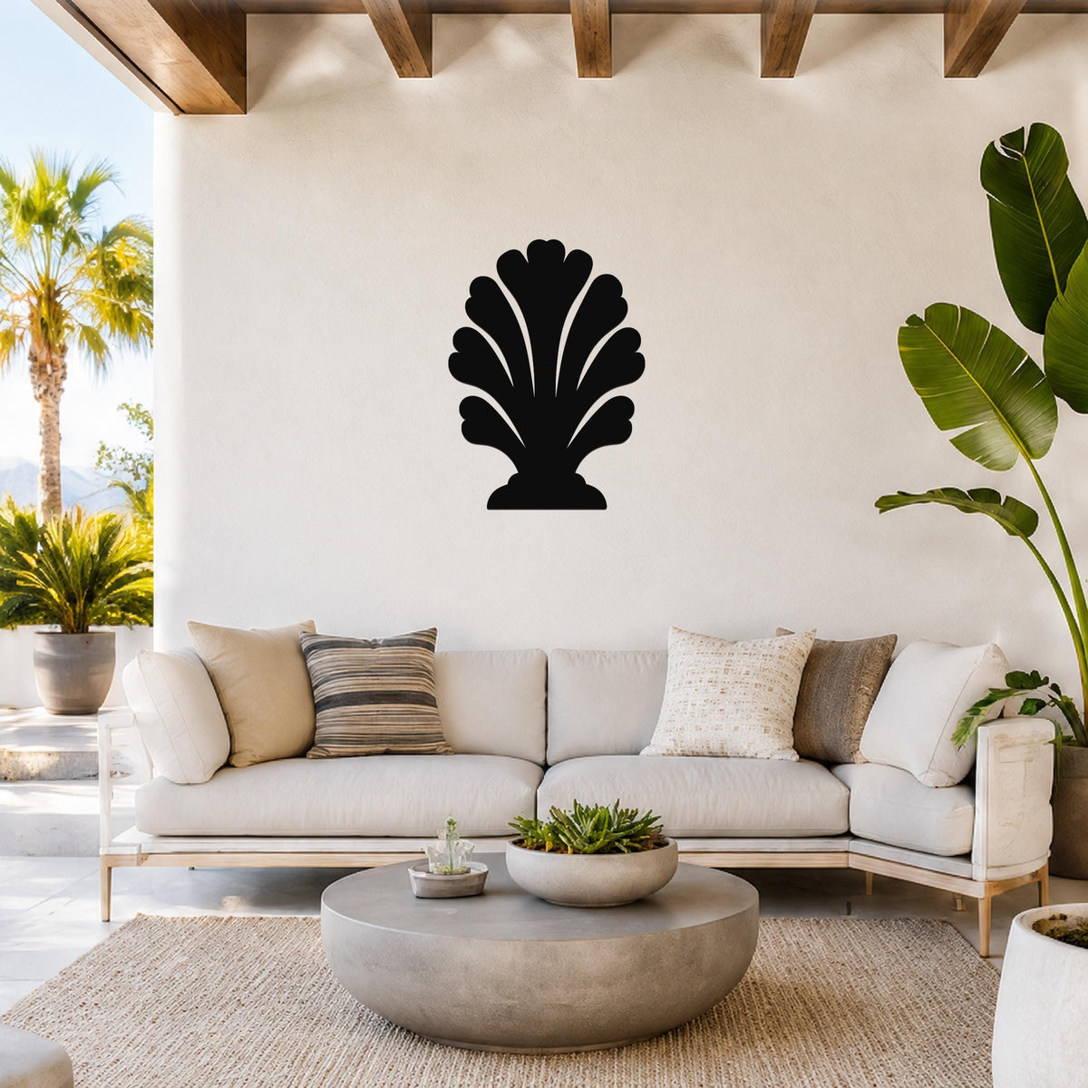 Black metal wall art in a coral or shell silhouette design, mounted on a white wall above a light-colored sofa in a bright, coastal-style living room.