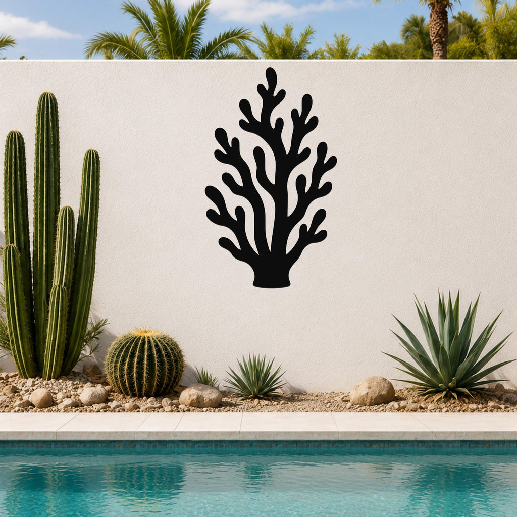 Black metal coral wall art with branching cutouts, mounted on a white outdoor wall beside a pool and desert plants.