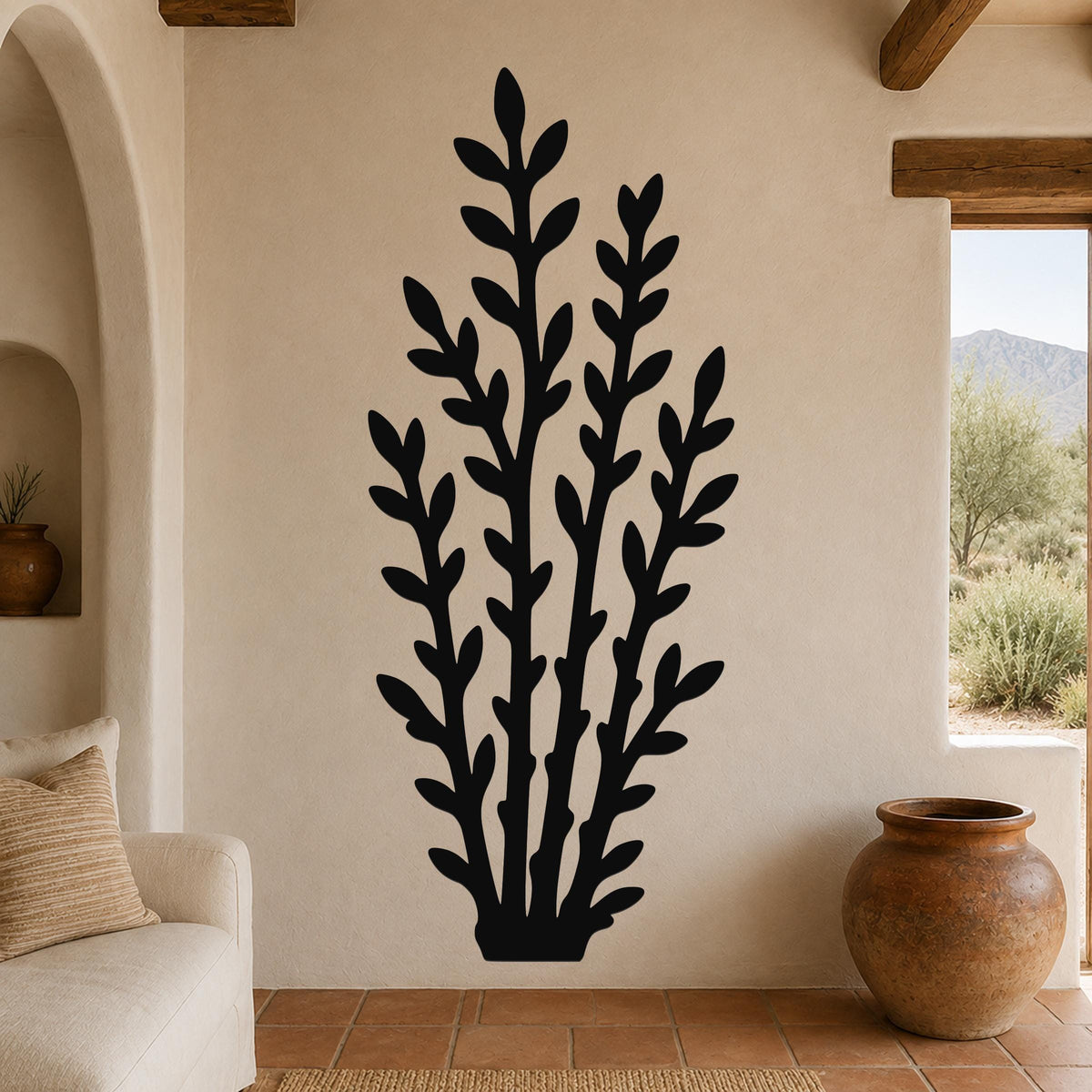 Black metal wall art with a leafy branch silhouette, mounted on a beige living room wall above a sofa.