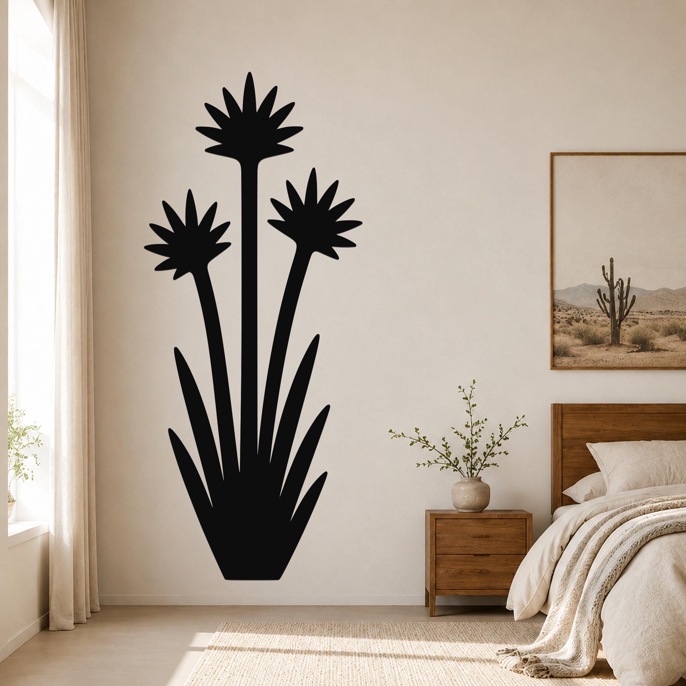 Black metal yucca wall art with three blooming flower silhouettes and long leaves, mounted on a bedroom wall above a wooden nightstand.