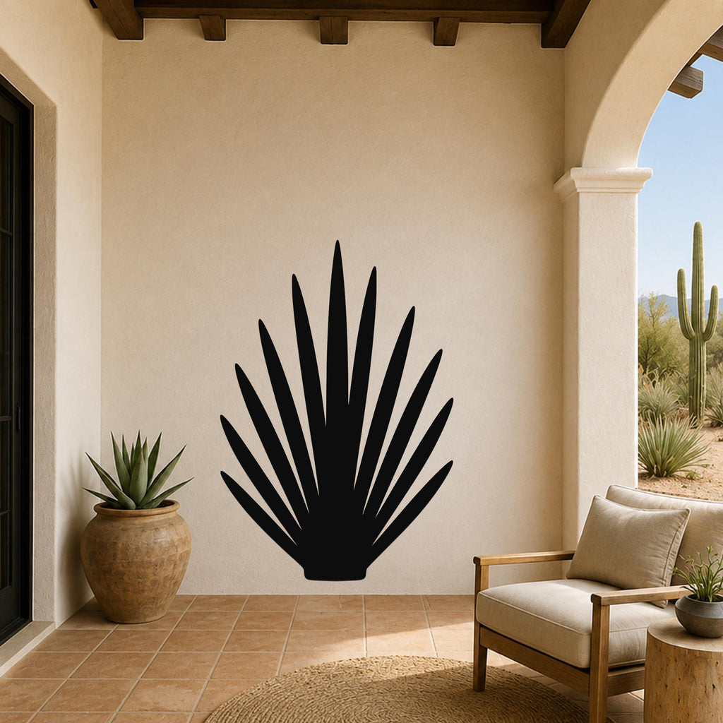 Black metal agave leaf wall art silhouette mounted on a beige stucco wall in a patio setting with arched entryway and desert view.