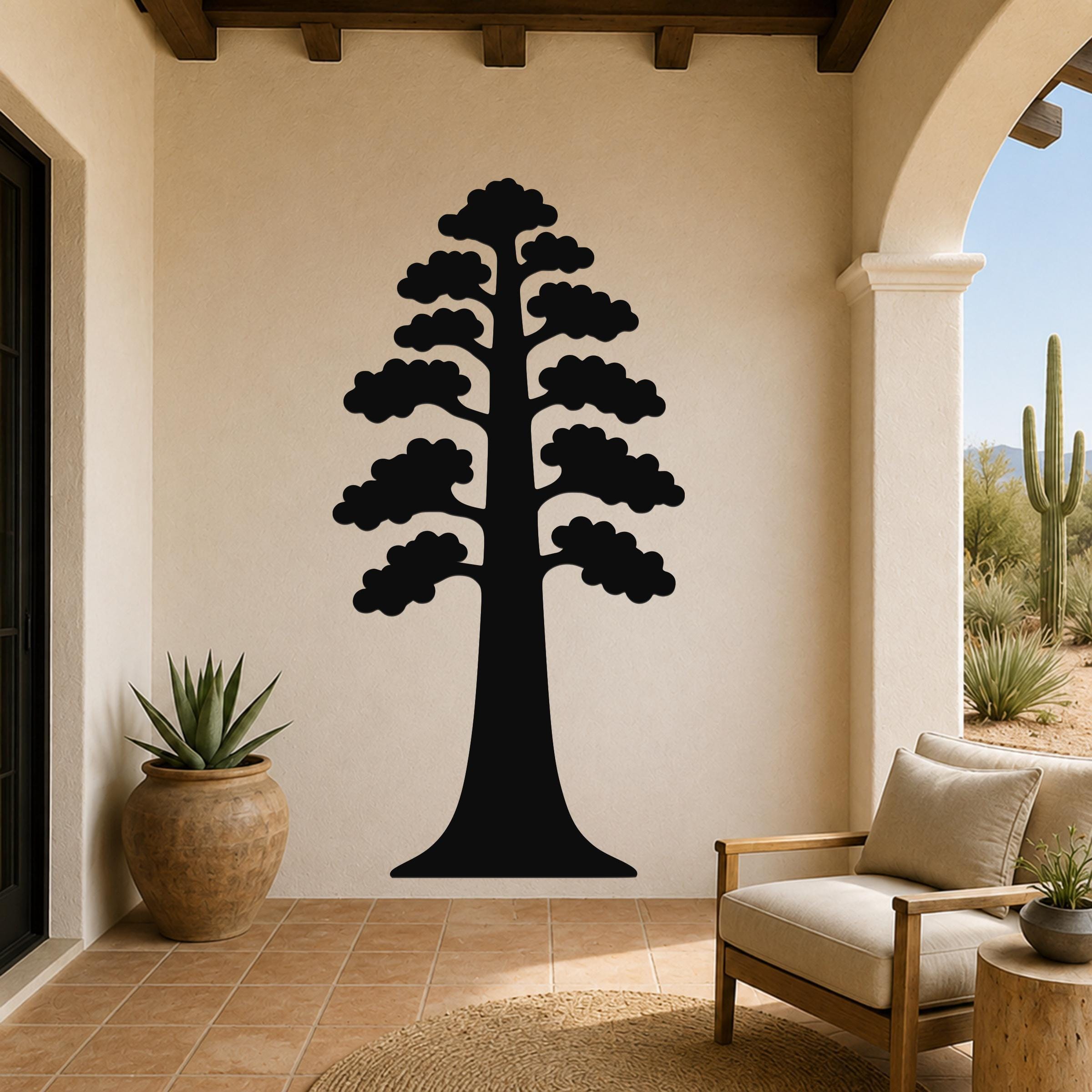Black metal wall art of a sequoia tree silhouette with layered branches, mounted on a beige stucco wall in a covered patio with arched entryway and desert view.