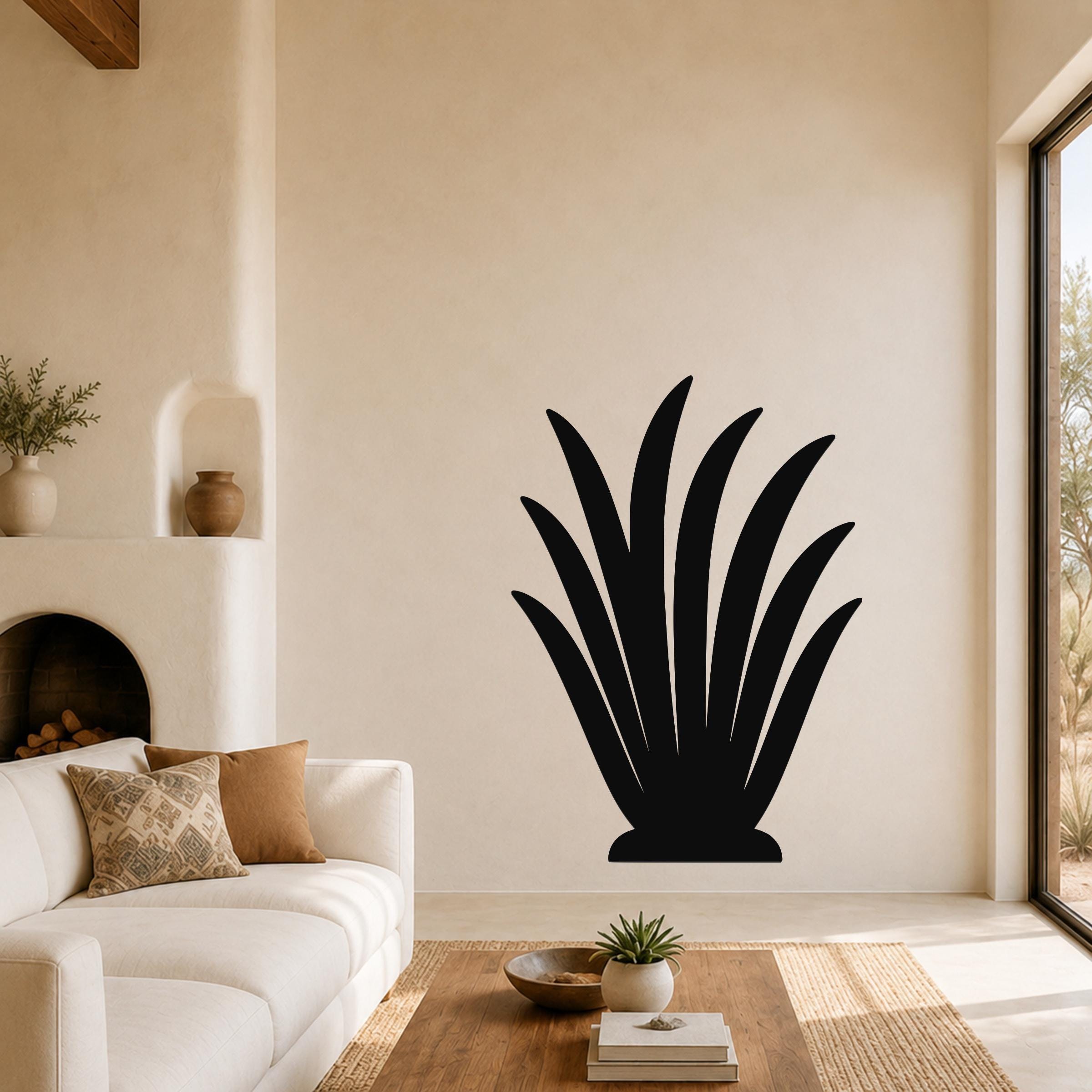 Black metal agave plant wall art with leaf cutouts, mounted on a living room wall above a coffee table.