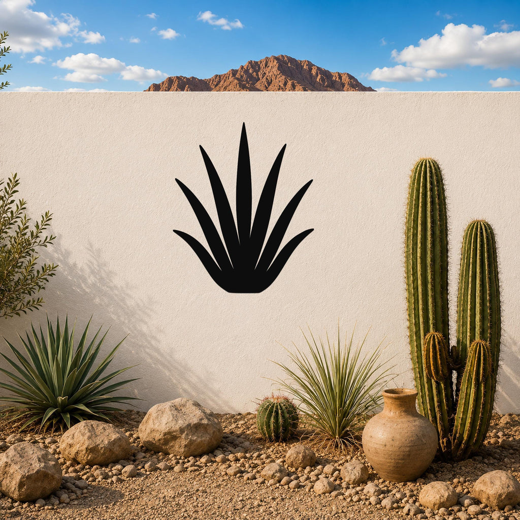 Black metal agave wall art silhouette mounted on a white outdoor wall above a desert garden with cacti and rocks.