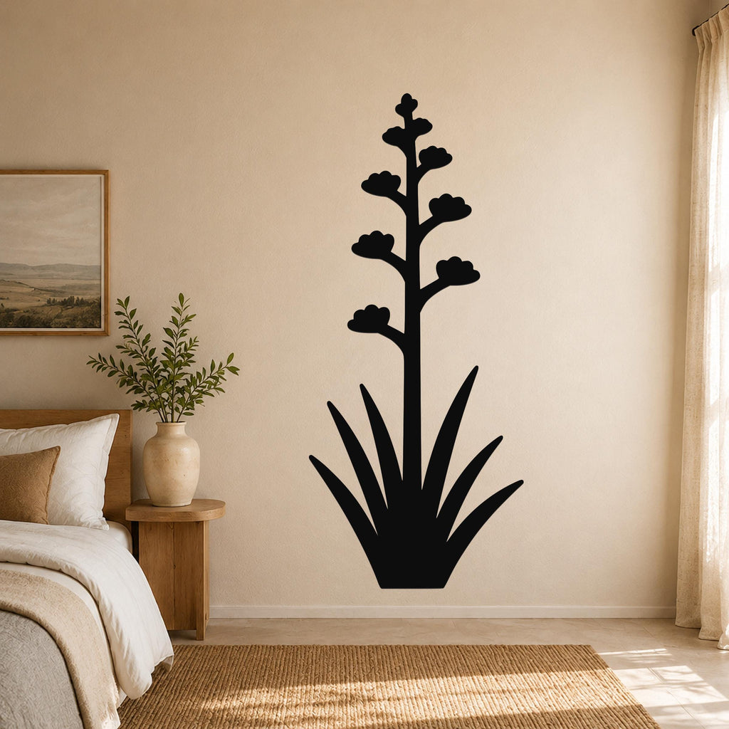 Black metal agave wall art with a tall flowering stalk and spiky leaves, mounted on a beige bedroom wall above a woven rug.