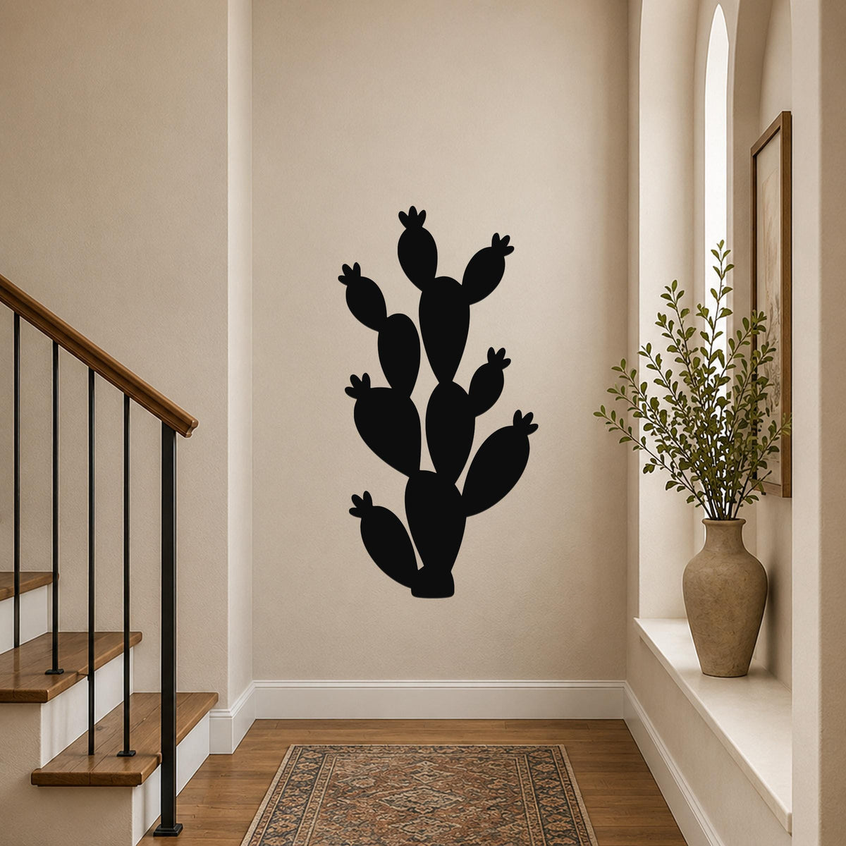 Black metal prickly pear cactus wall art with multiple segmented pads and small flower cutouts, mounted on a hallway wall above a patterned rug near a staircase.