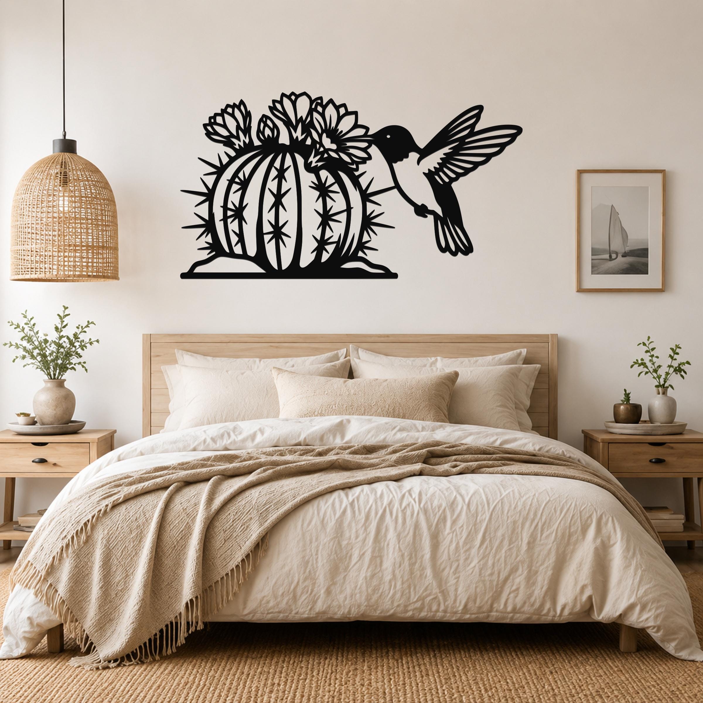 Black metal wall art featuring a hummingbird and flowering barrel cactus cutout, mounted above a bed in a neutral bedroom.