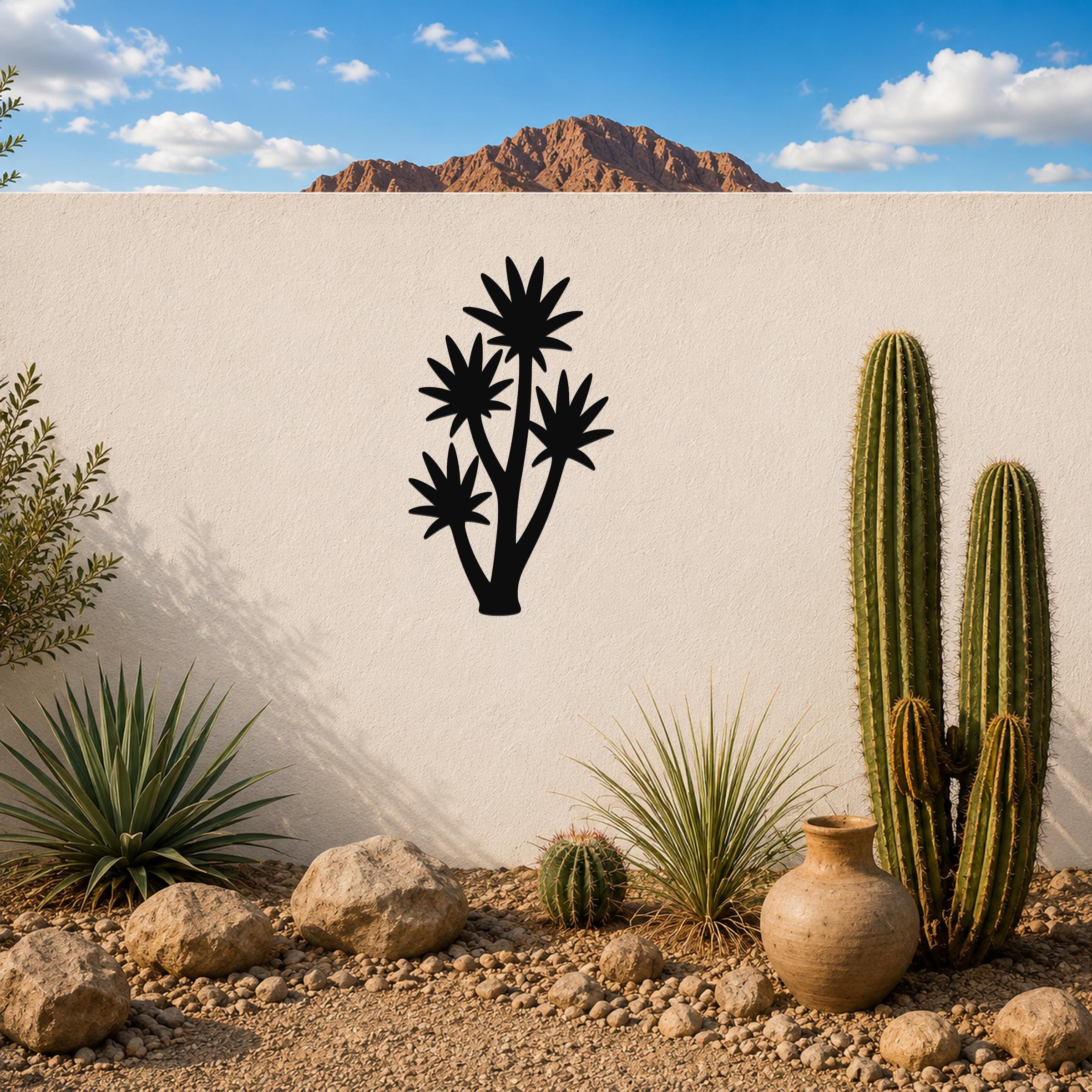 Black metal yucca wall art with multiple star-shaped cutouts, mounted on a white outdoor wall above a desert garden with cacti and rocks.