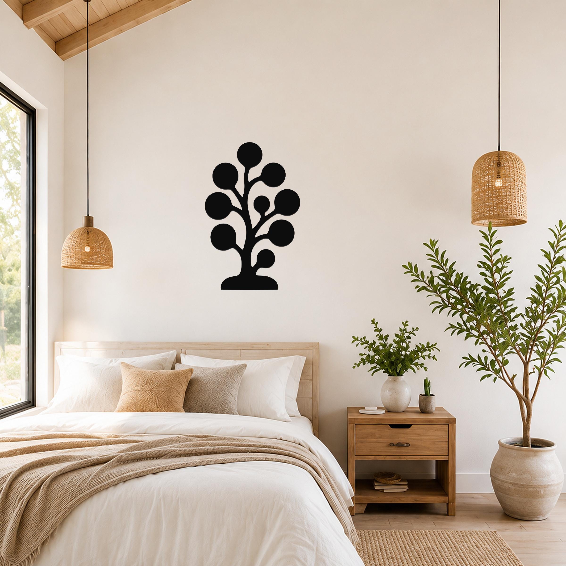 Black metal wall art in a tree silhouette with circular leaf shapes, mounted on a bedroom wall above a bed.