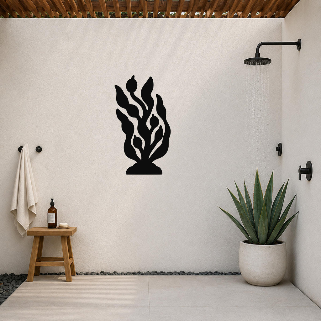 Black metal kelp and seaweed wall art with leafy cutouts, mounted on a white outdoor shower wall above a potted succulent.