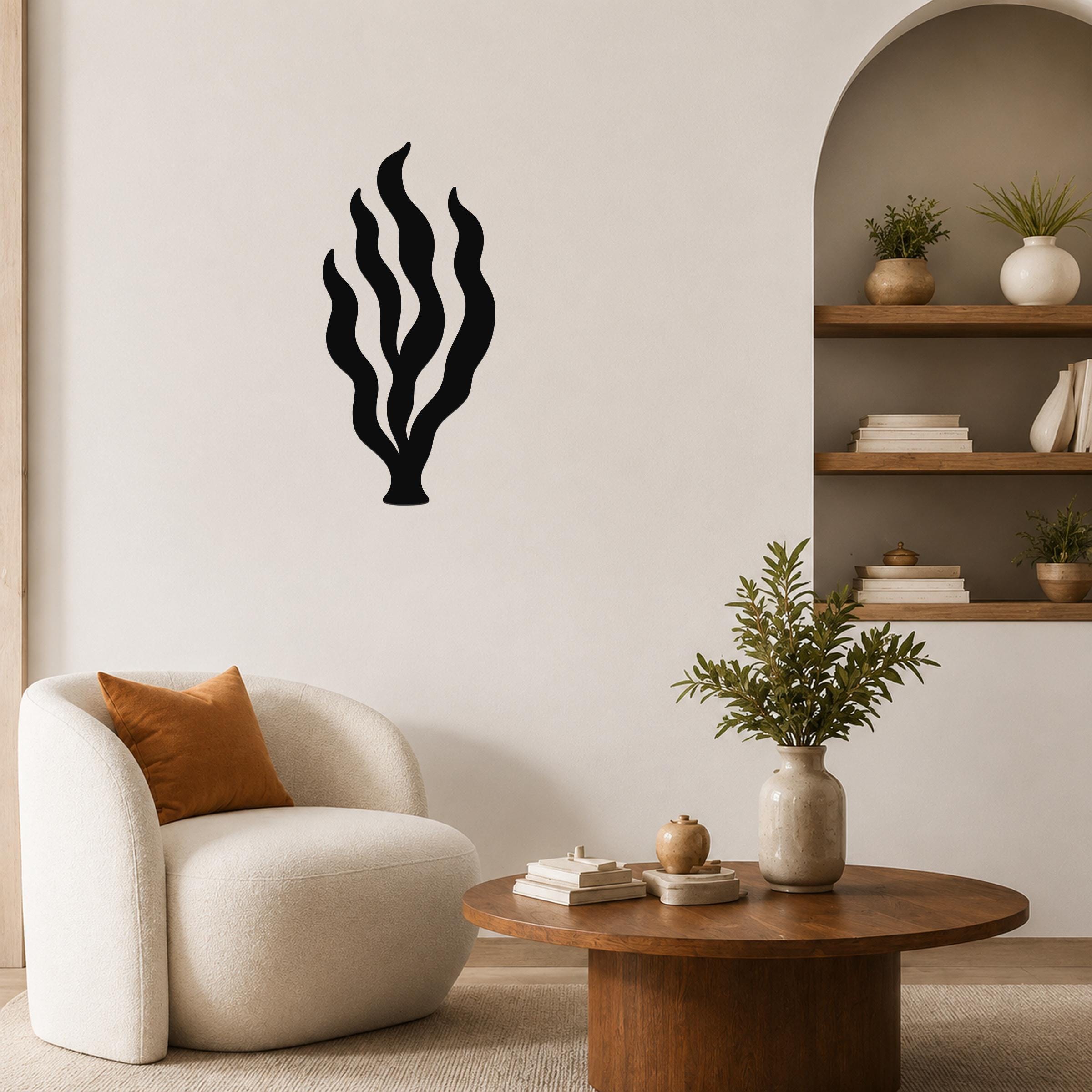 Black metal kelp seaweed wall art with flowing frond cutouts, mounted on a living room wall above a round wooden coffee table.