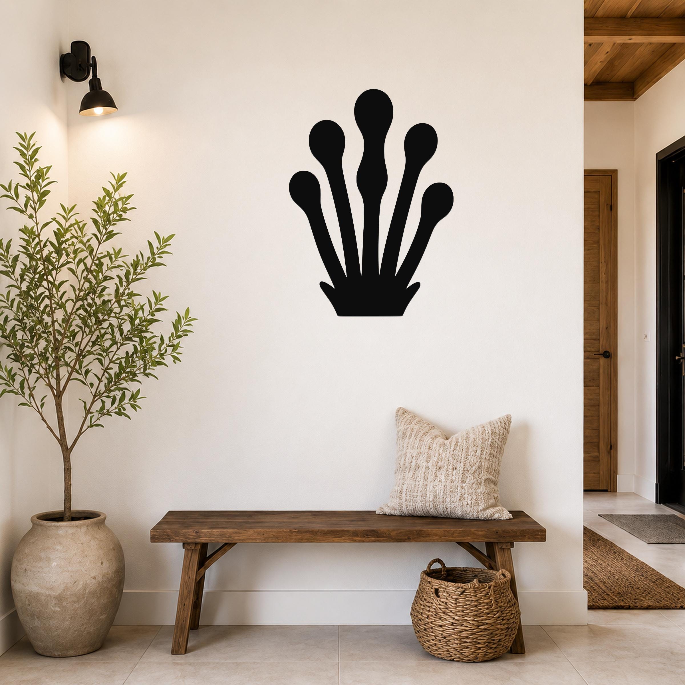 Black metal wall art in a kelp or seaweed silhouette, mounted on a white wall above a wooden bench in a modern entryway.