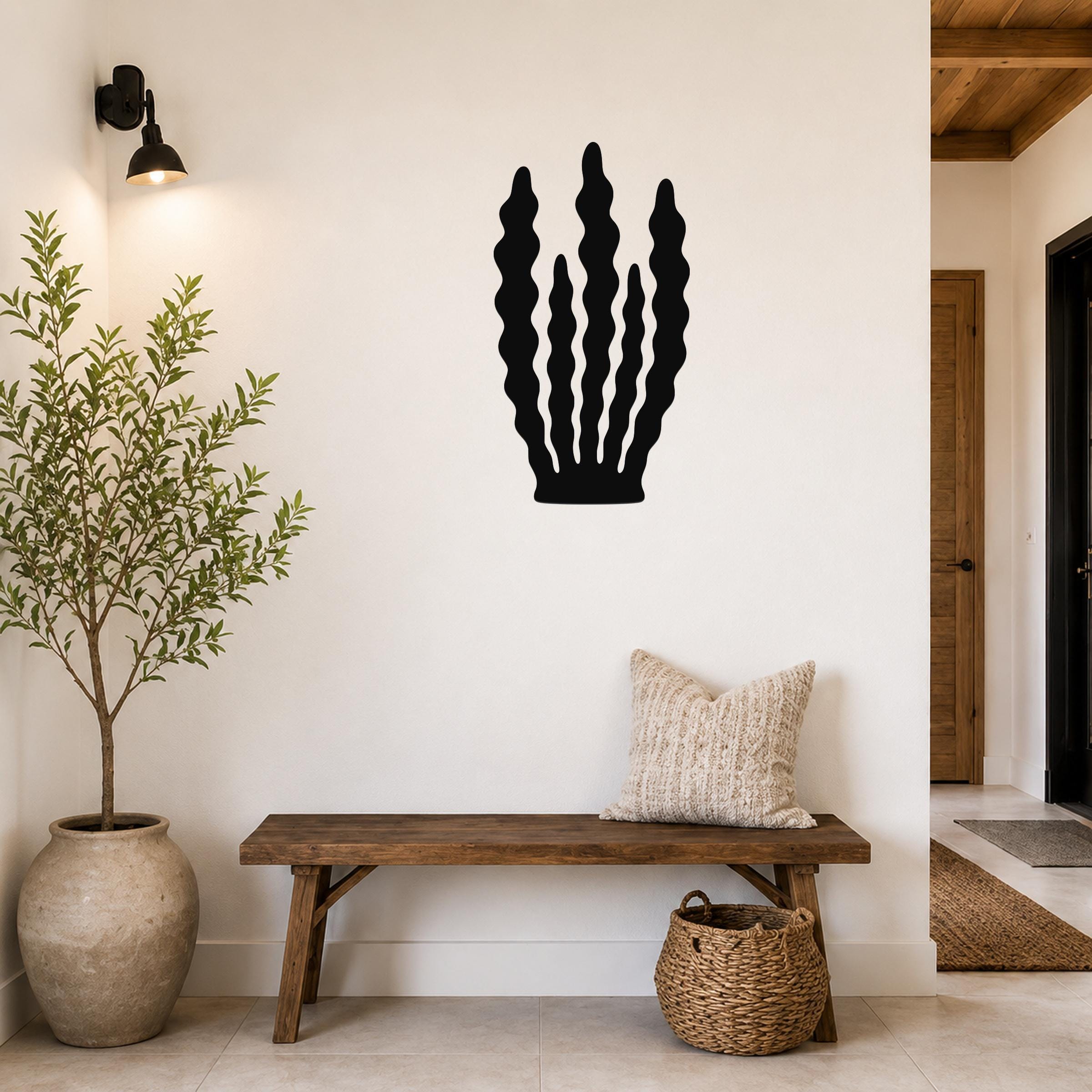 Black metal kelp wall art with wavy vertical cutouts, mounted on a white wall above a wooden bench in a entryway.