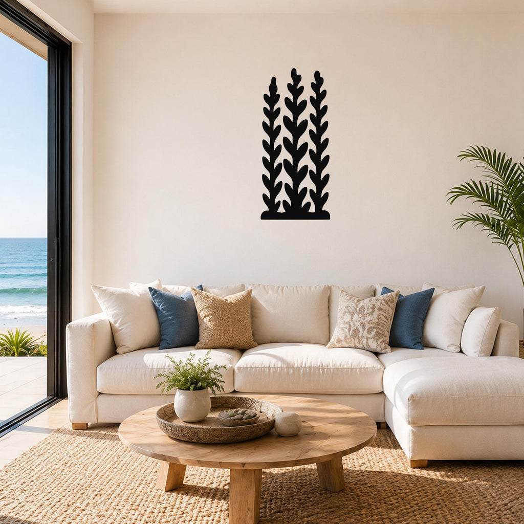 Black metal wall art with a kelp and seaweed silhouette design, mounted on a living room wall above a white sofa.