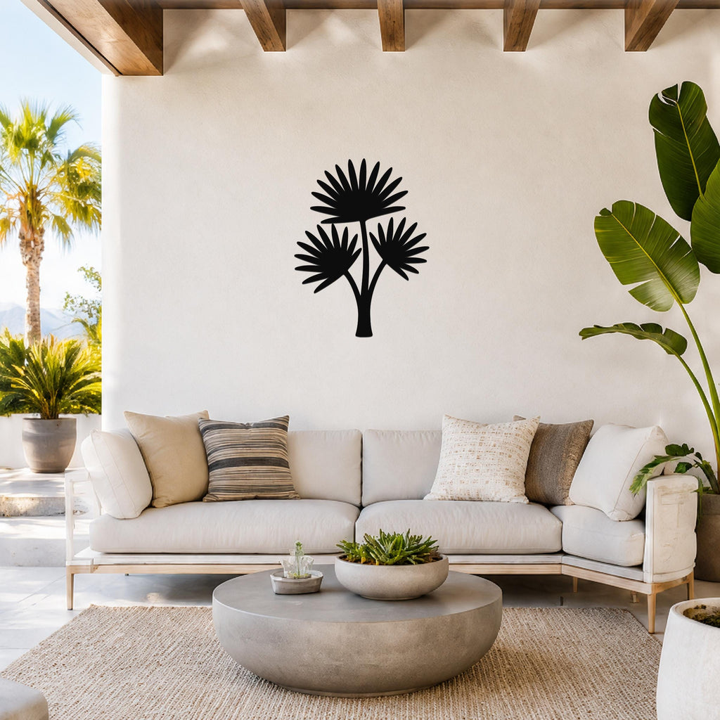 Black metal cutout palm tree wall art with three fan-shaped fronds, mounted on a white wall above a light-colored sofa in a bright living room.