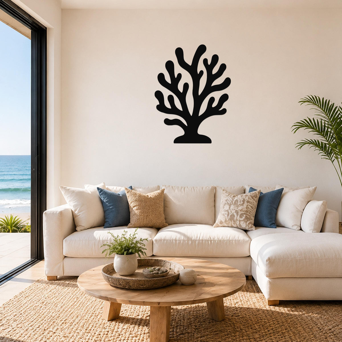 Black metal coral wall art with branching cutouts, mounted above a white sofa in a living room with ocean views.