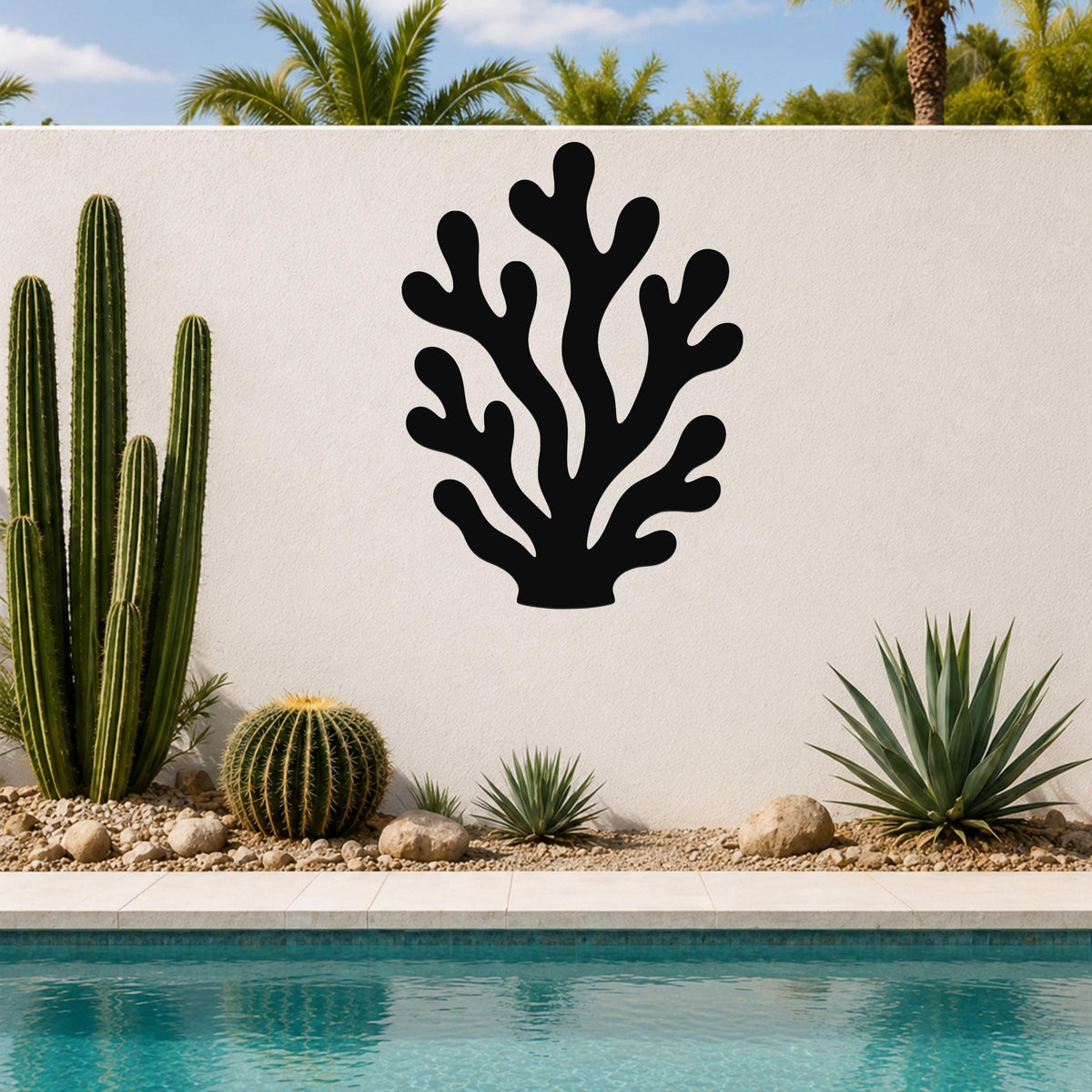 Black metal coral wall art with branching cutouts, mounted on an outdoor wall beside a pool and cacti.