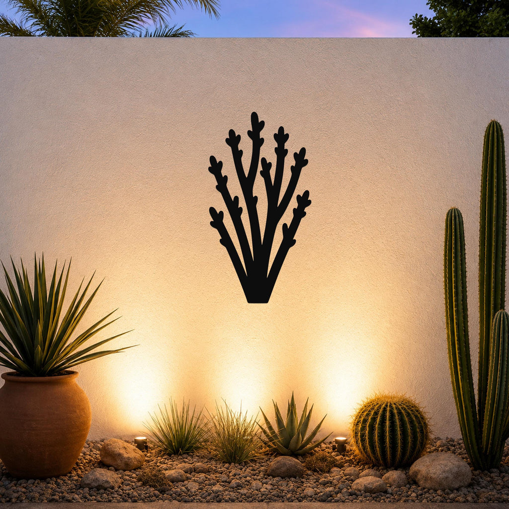 Black metal wall art in a desert branch silhouette, mounted on an outdoor wall above a gravel garden with cacti and warm uplighting.