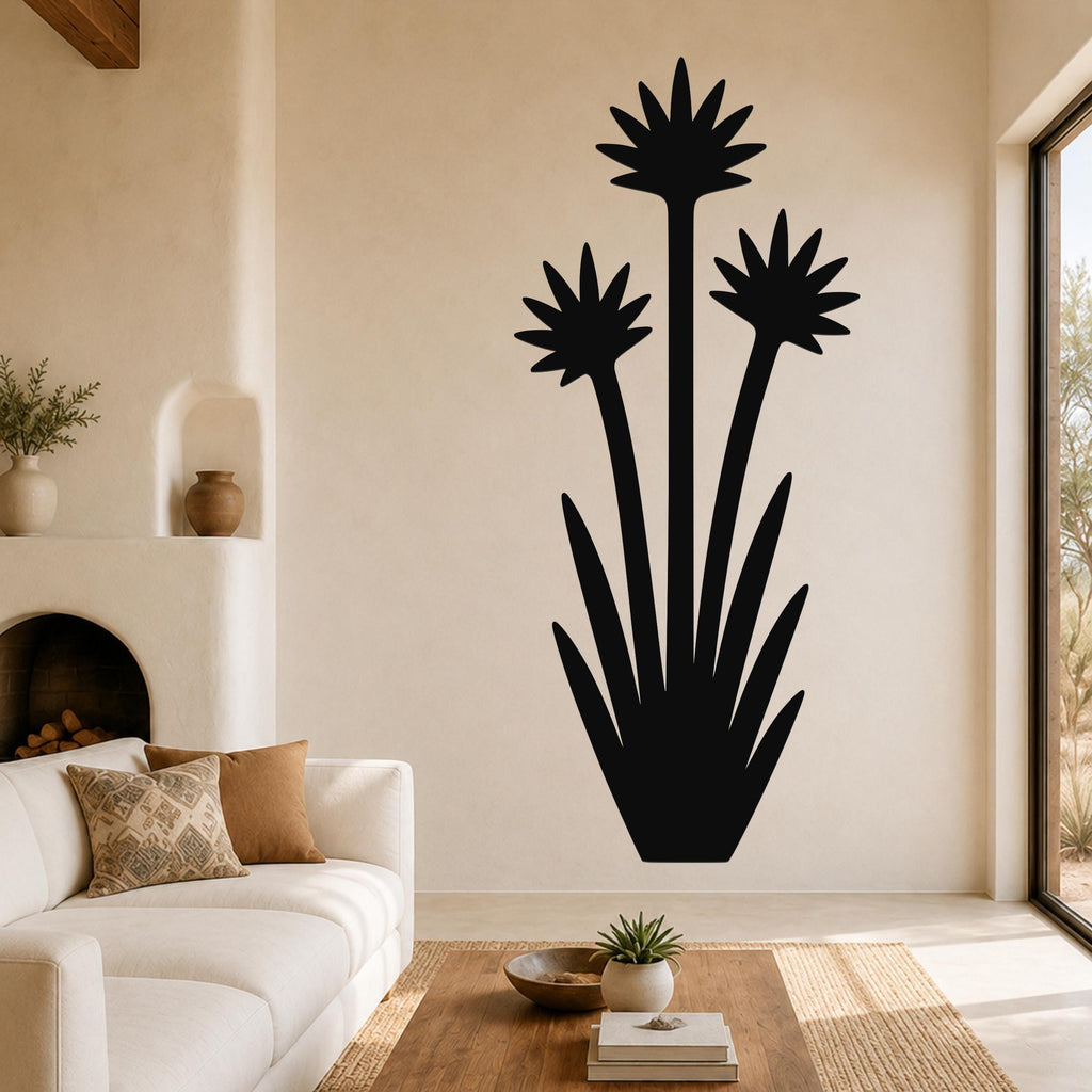 Black metal wall art silhouette of a blooming yucca plant with three star-shaped flower heads and long spiky leaves, mounted on a living room wall above a sofa.