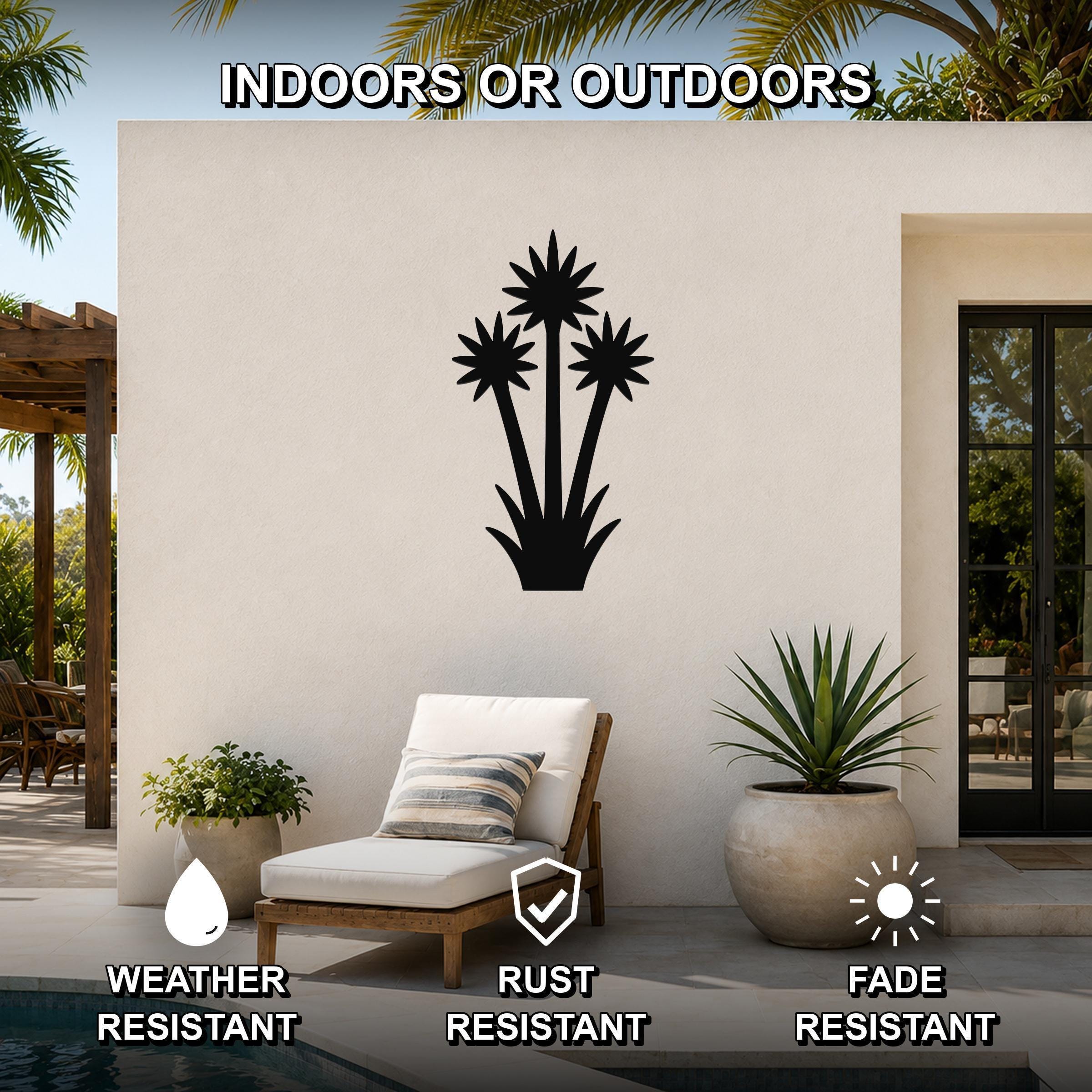 Black metal wall art featuring a yucca plant silhouette with three starburst flowers and spiky leaves, mounted on an outdoor patio wall above a lounge chair.