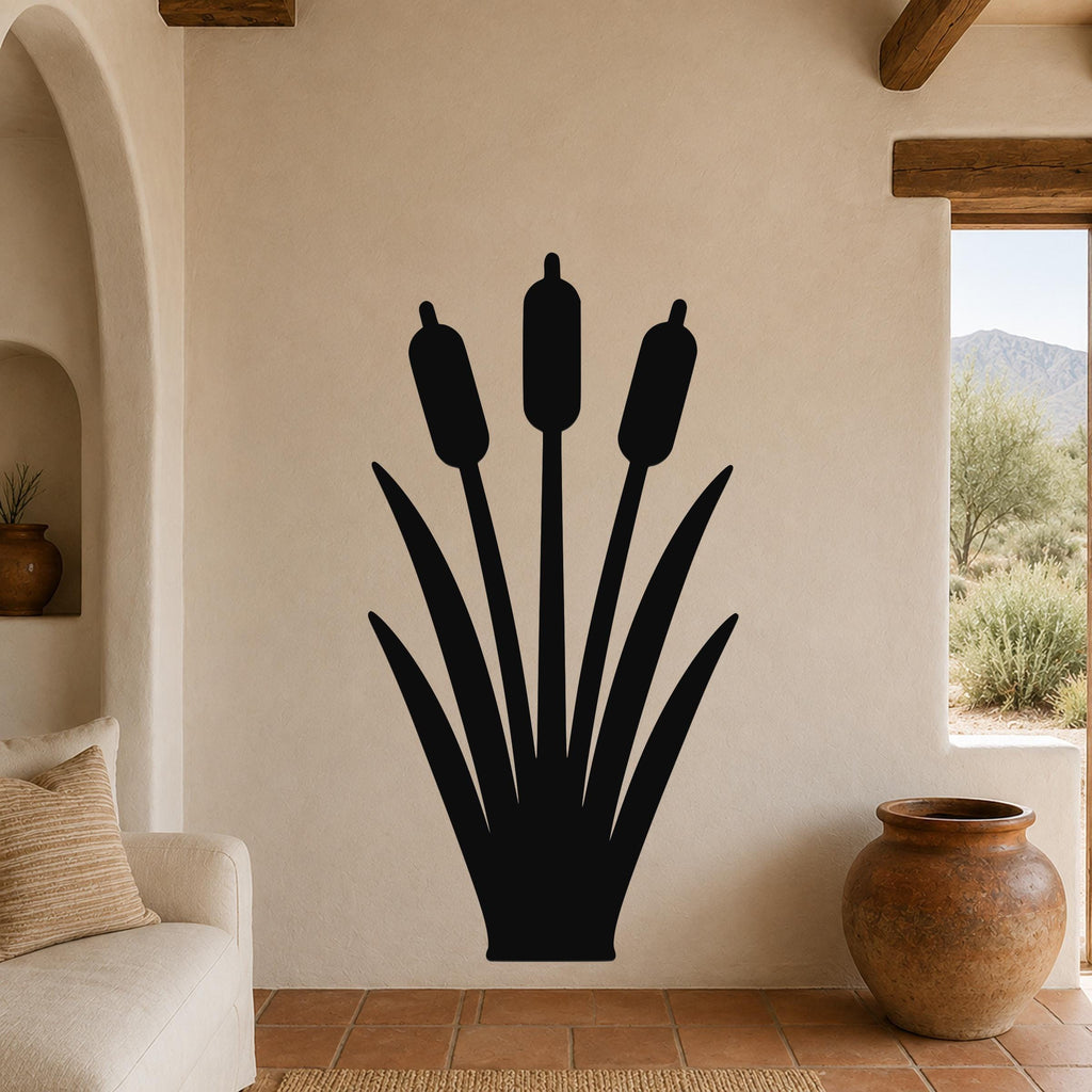 Black metal cattail wall art silhouette with three seed heads and long leaves, mounted on a beige living room wall above a sofa.