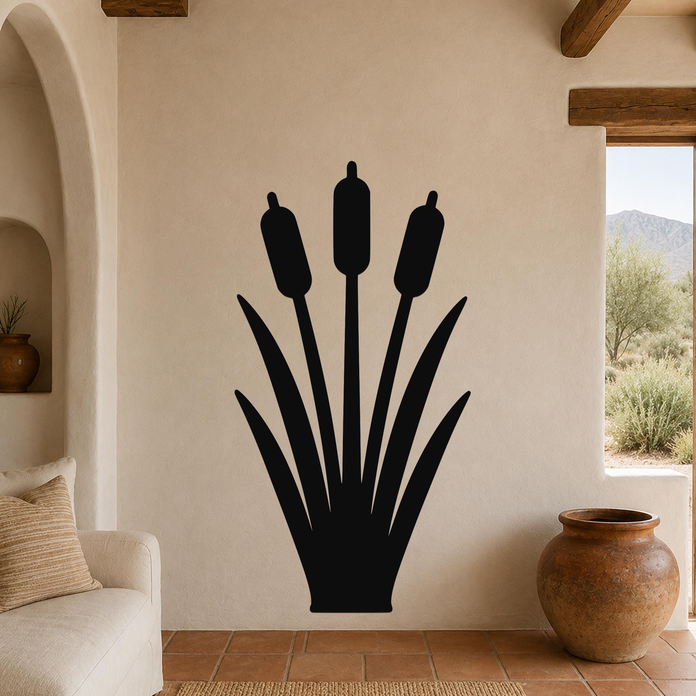 Black metal cattail wall art silhouette with three seed heads and long leaves, mounted on a beige living room wall above a sofa.