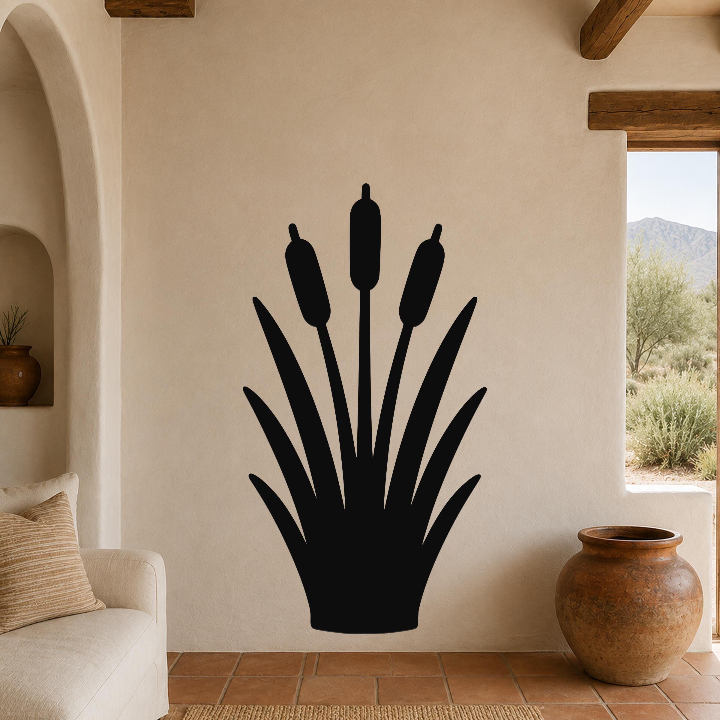 Black metal cattail wall art silhouette with three seed heads and long leaves, mounted on a beige living room wall above a sofa.