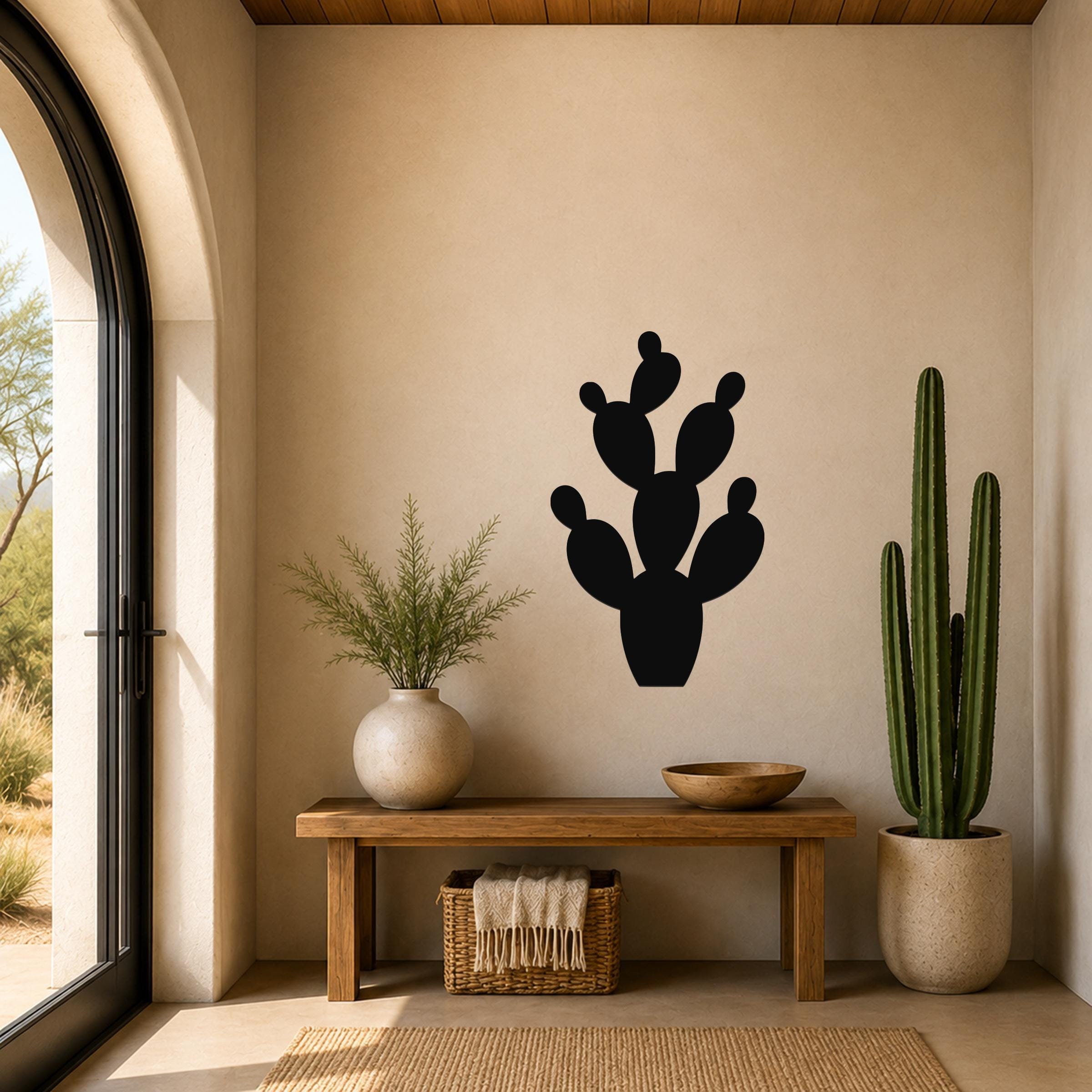 Black metal prickly pear cactus wall art with multiple rounded pads and cutout details, mounted on a beige wall above a wooden bench in a sunlit entryway.