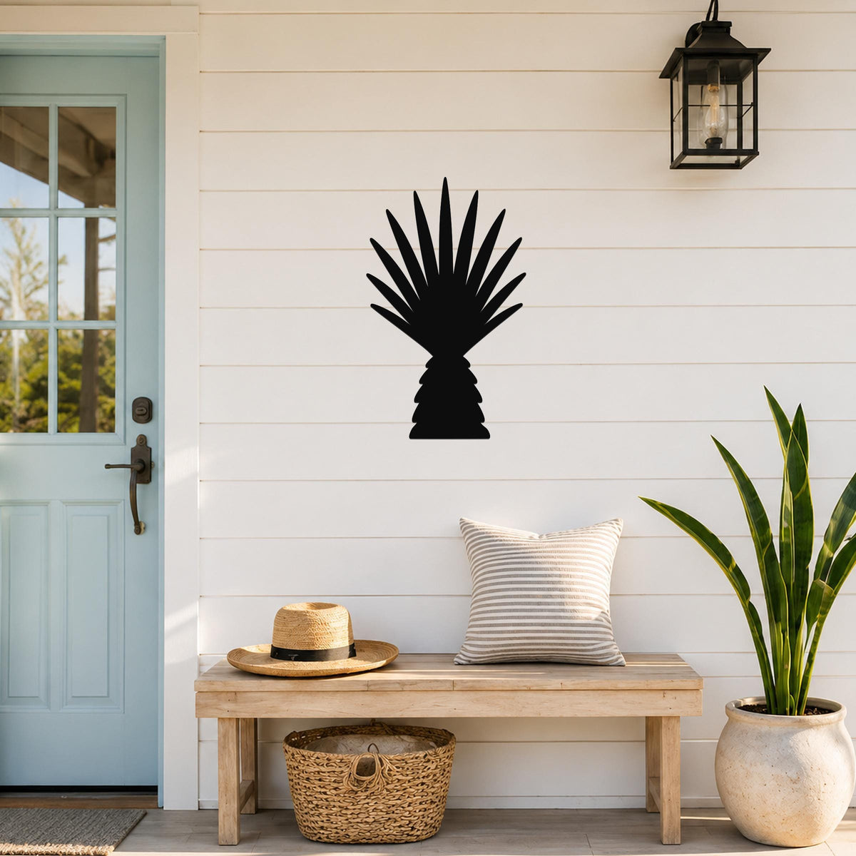 Black metal palm tree wall art with fan-shaped fronds, mounted on a white shiplap wall above a wooden bench on a porch.