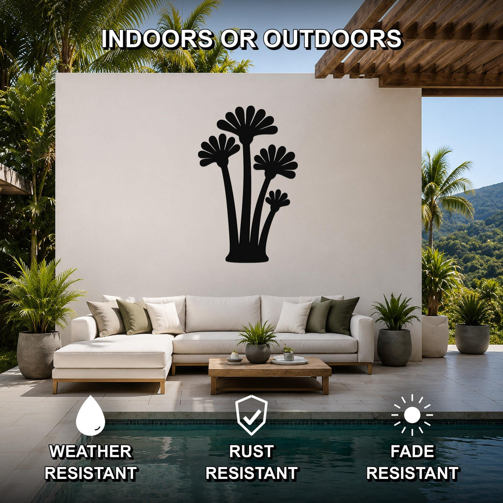 Black metal palm tree wall art with fan-shaped fronds, mounted on a white outdoor wall above a sofa in a patio living area.