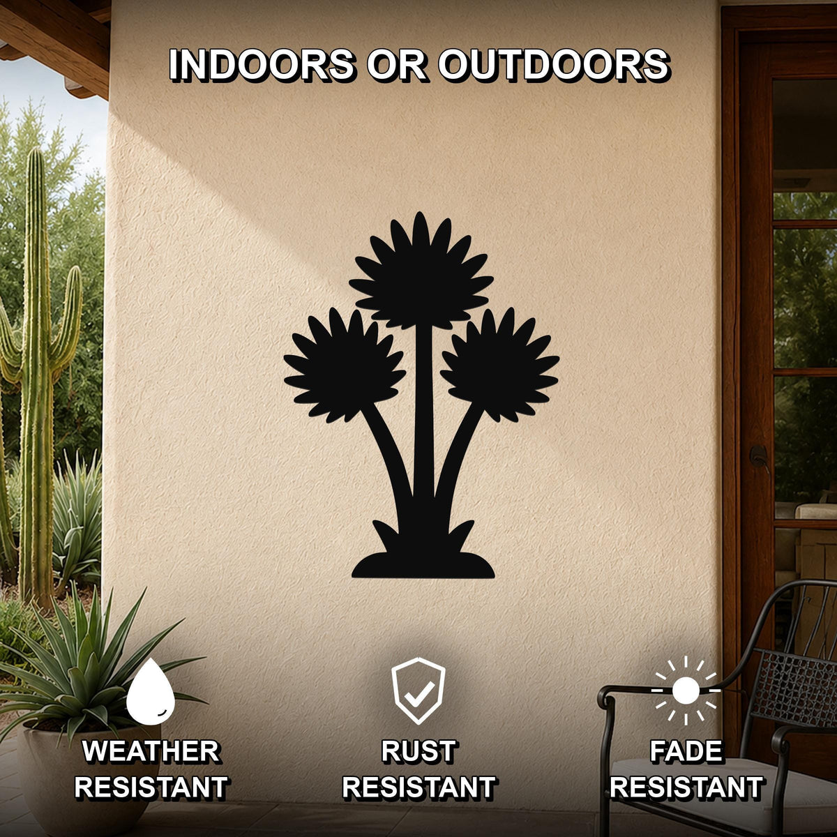 Black metal wall art featuring a silhouette of three desert flowers, mounted on an outdoor patio wall with cacti and a chair visible nearby.