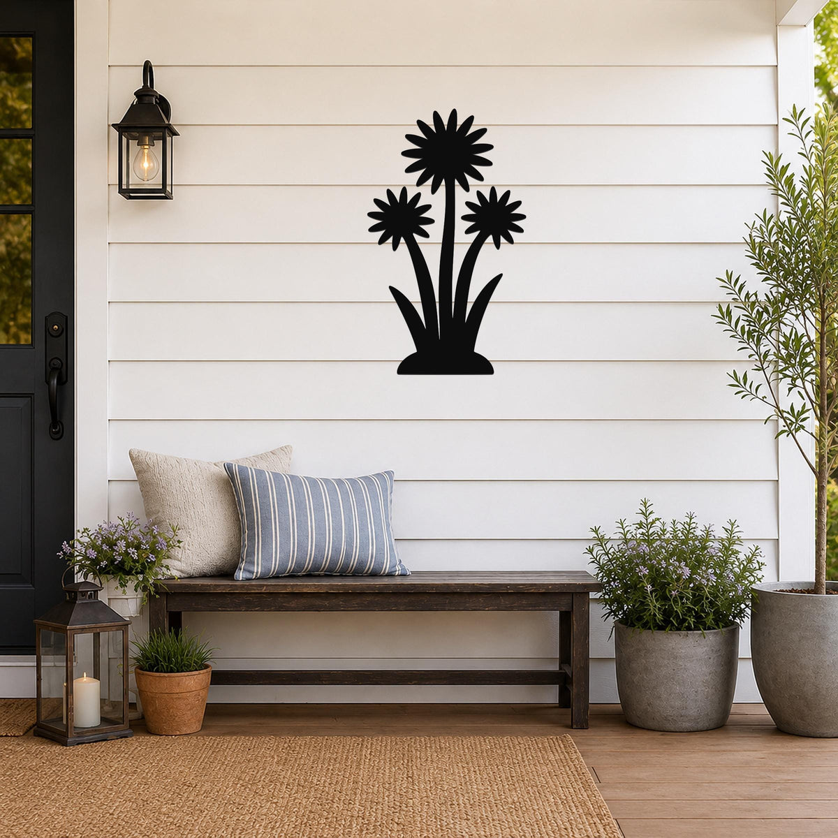 Black metal wall art featuring a silhouette of three wildflowers with layered petals and long stems, mounted on a white shiplap wall above a wooden bench on a porch.
