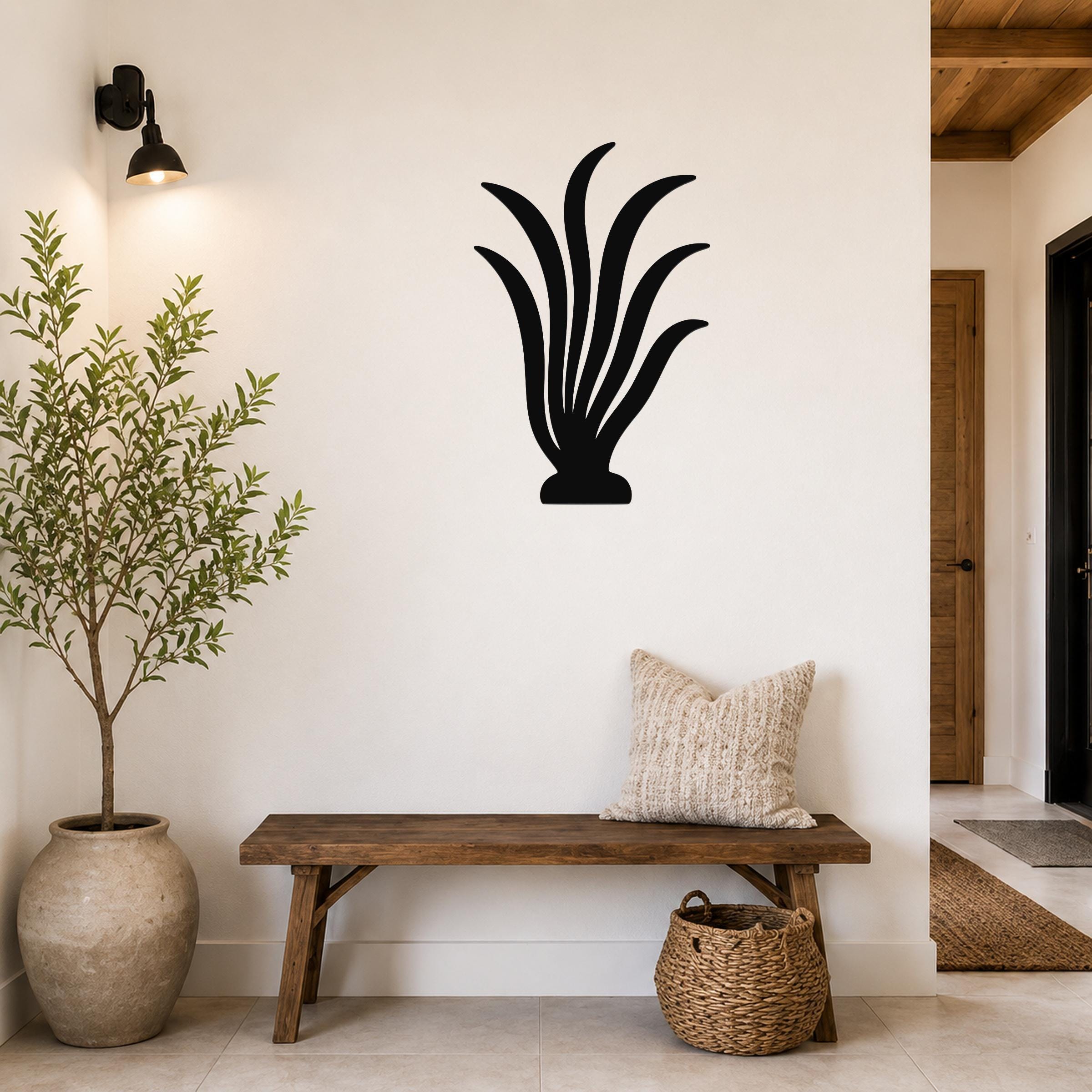 Black metal kelp wall art with flowing leaf cutouts, mounted on a white wall above a wooden bench in a modern entryway.