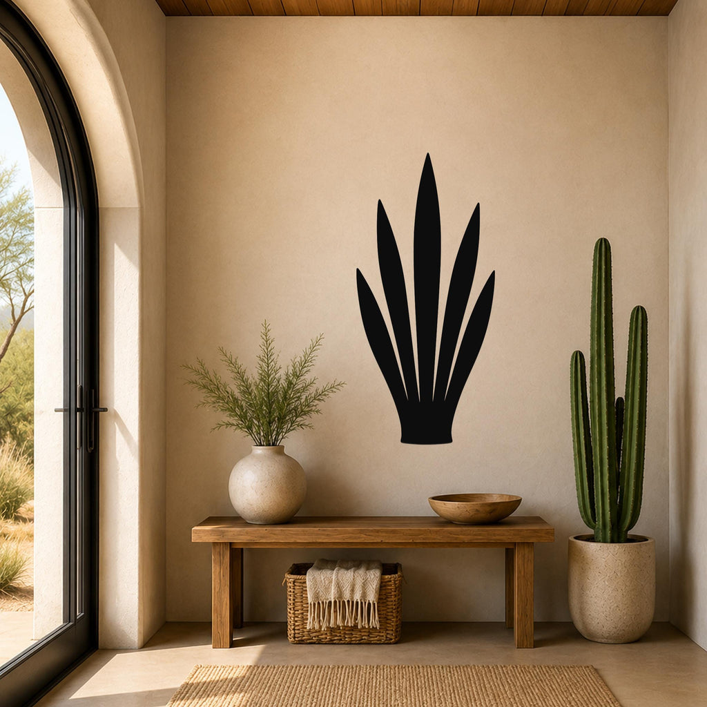 Black metal agave leaf wall art silhouette mounted on a beige wall above a wooden bench in a sunlit entryway.
