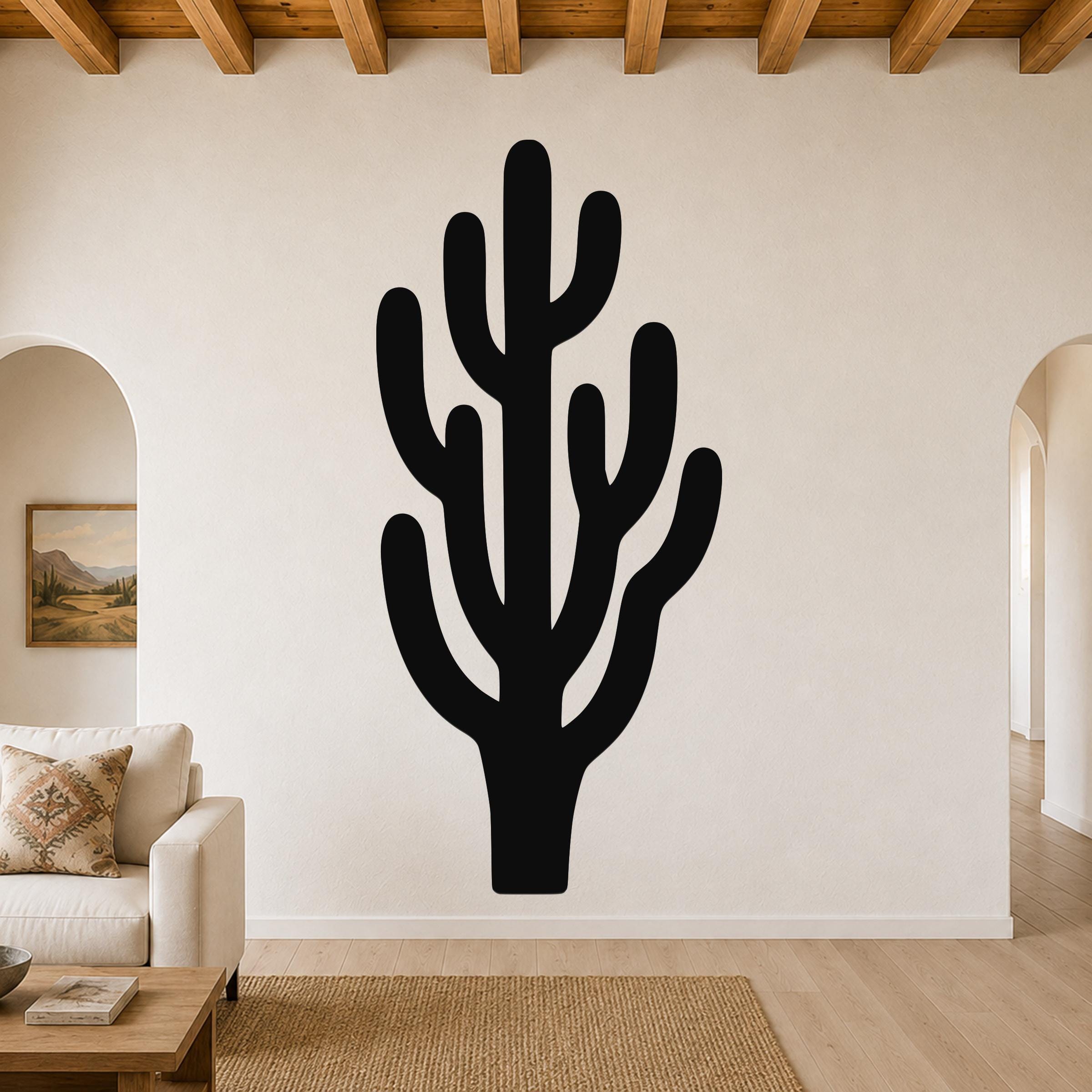 Black metal saguaro cactus wall art with branching cutouts, mounted on a living room wall above a sofa.